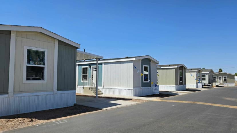 A row of newly built manufactured homes with tan and blue-gray siding, some marked sold and for sale,